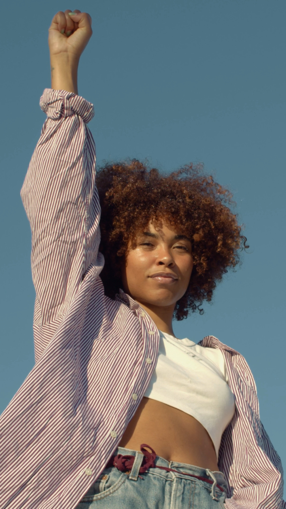 portrait of two mixed-race women with huge afro hair makes a protest black raised fist gesture outdoors portrait on the sky background