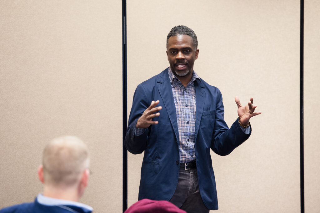 man in professional outfit gestures while talking to group of people